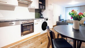 A modern kitchen with stainless steel appliances, a built-in oven, and a microwave. There's a dining area with a round table and chairs, and a vase with flowers on the table. - Schiffmeisterapartment Melk, Wachau - design meets history (Melk)
