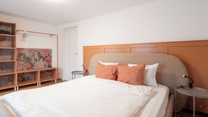A bedroom with a bed, a wooden headboard, a side table, and a shelving unit with floral-patterned fabric. - Schiffmeisterapartment Melk, Wachau - design meets history (Melk)
