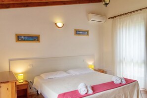 A hotel room with a large bed, two bedside lamps, a nightstand, a wooden headboard, and two framed pictures on the wall. - San Giuliano Two-room apartment 4 beds standard (Alghero)