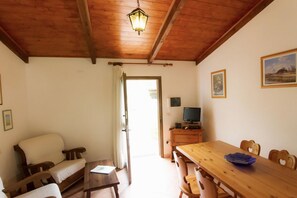 Una stanza accogliente con soffitto in legno, un tavolo da pranzo con sedie, un divano, un televisore su un mobiletto in legno e una porta che dà all'esterno.