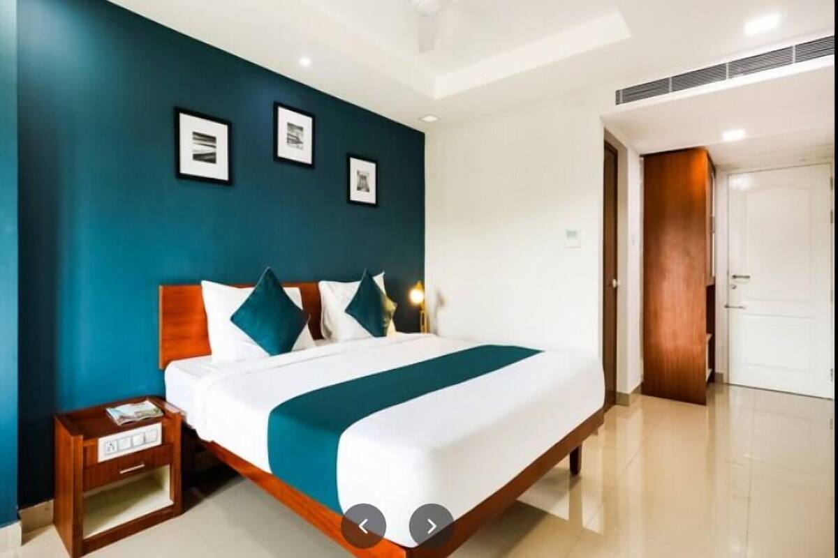 A modern hotel room with a large bed, a nightstand, and a door to the right.