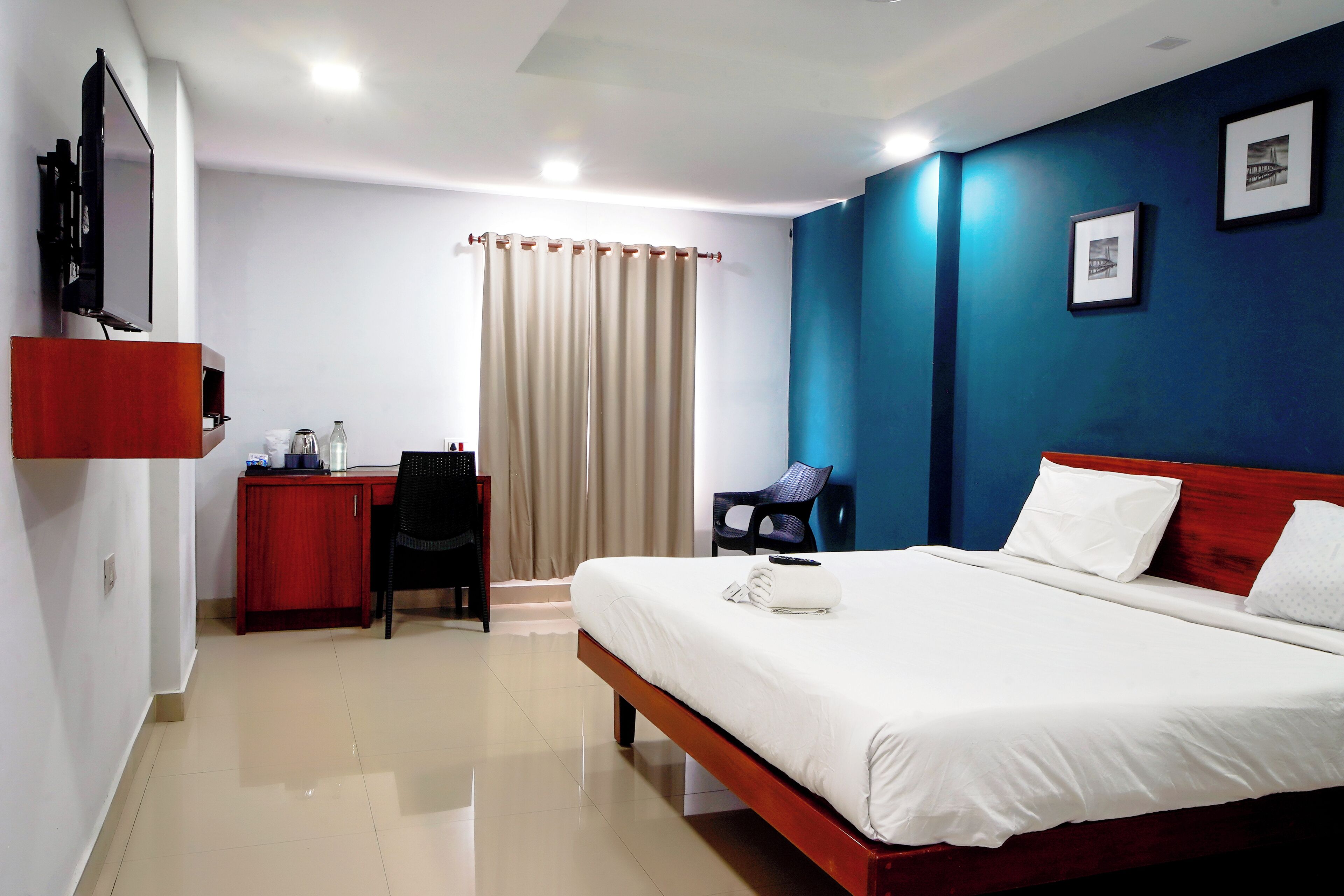 A hotel room with a bed, a desk, a chair, a TV, and a curtain.