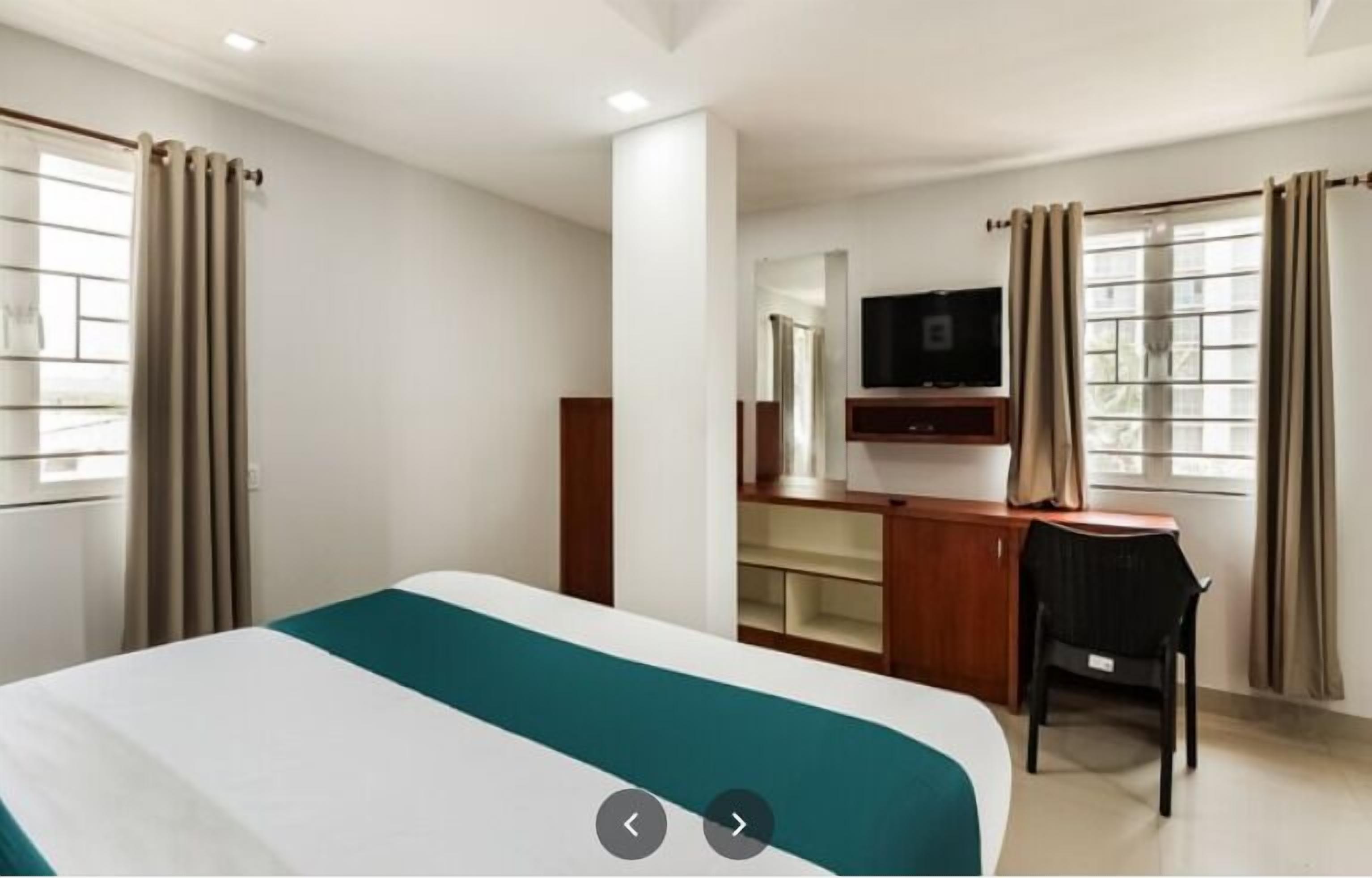 A hotel room with a bed, a desk, a chair, a television, and a window with curtains.
