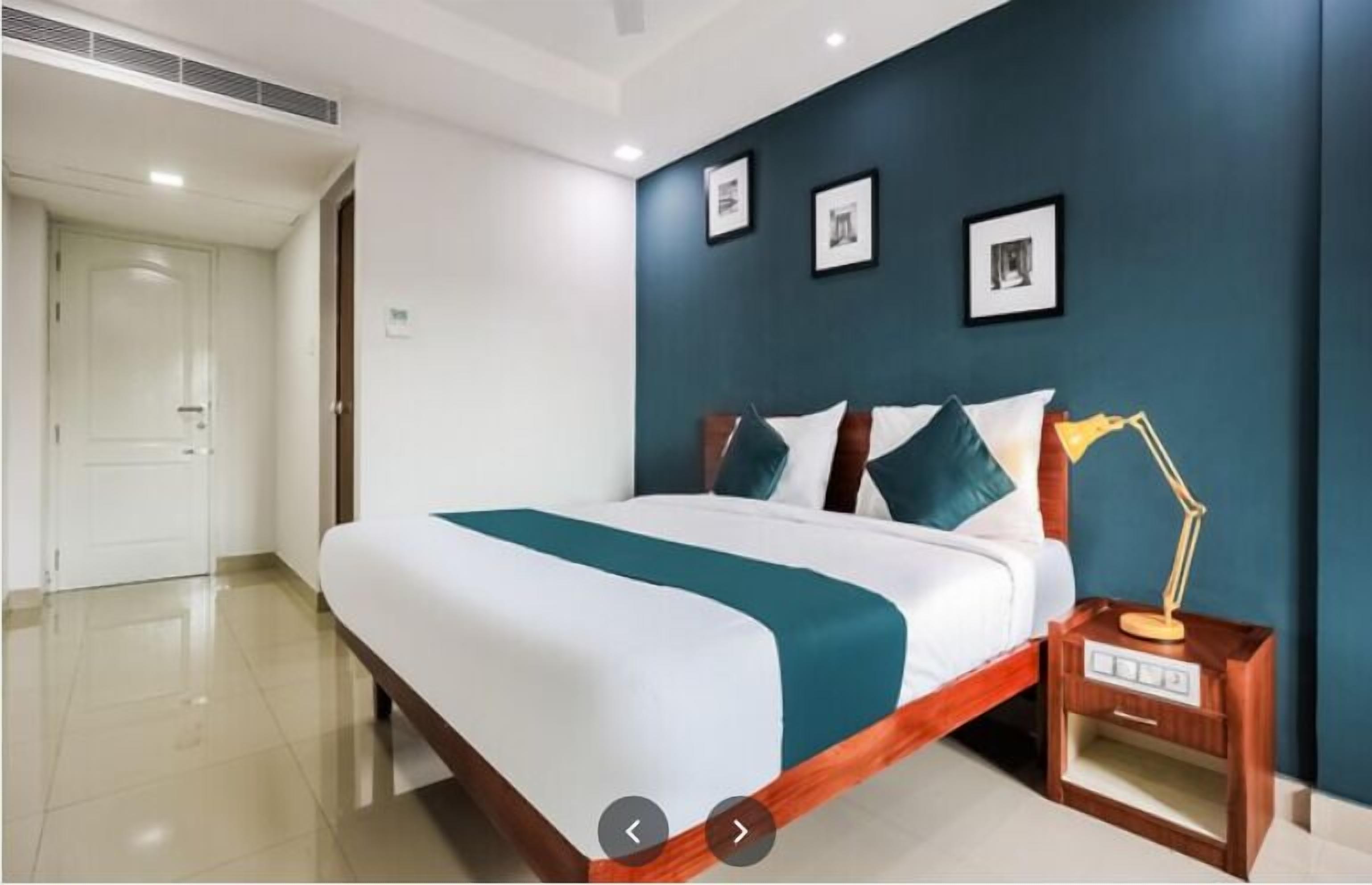 Een moderne hotelkamer met een groot bed, een nachtkastje met een lamp en een donkerblauwe accentmuur met ingelijste foto's.