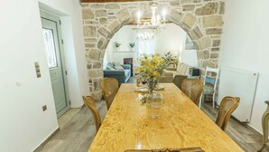 A dining area with a wooden table, six wicker chairs, a chandelier, and a stone archway. - Villa Simantiri - Romantic Luxury Villa with jacuzzi & sunset views (Pompia)