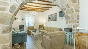 A cozy living room with stone walls, wooden beams, a chandelier, and a variety of seating options. - Villa Simantiri - Romantic Luxury Villa with jacuzzi & sunset views (Pompia)