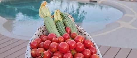 A bowl of tomatoes and zucchini on a wooden deck by a pool.