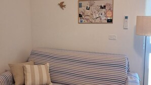 Un canapé à rayures avec un coussin, un tableau d’affichage avec des papiers et une horloge, et une lampe sur une table.