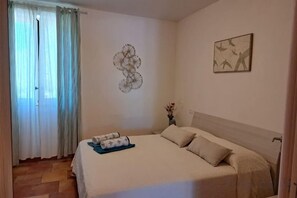 Un dormitorio con cama, cortinas, un adorno de pared y un cuadro.