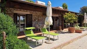 Un bâtiment en pierre doté d’un patio aménagé avec des fauteuils de jardin verts et des parasols blancs.