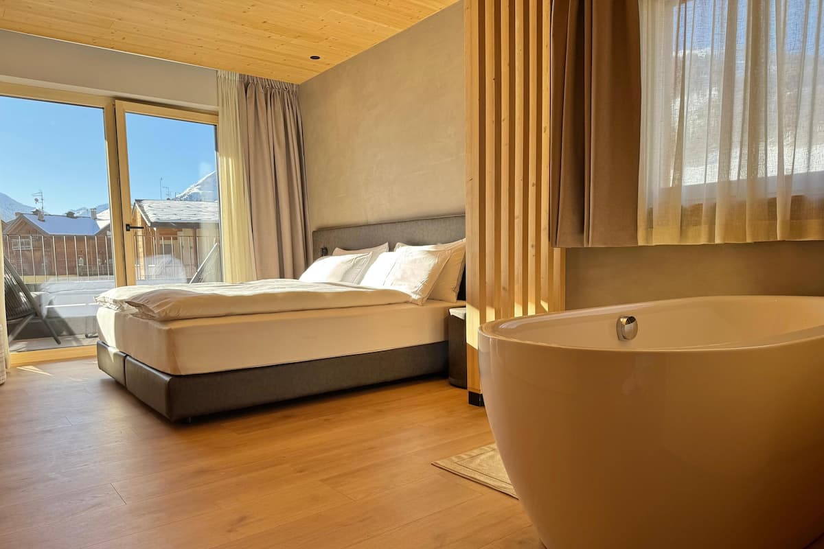 Un dormitorio moderno con una cama grande, una bañera y vistas a montañas desde la ventana.