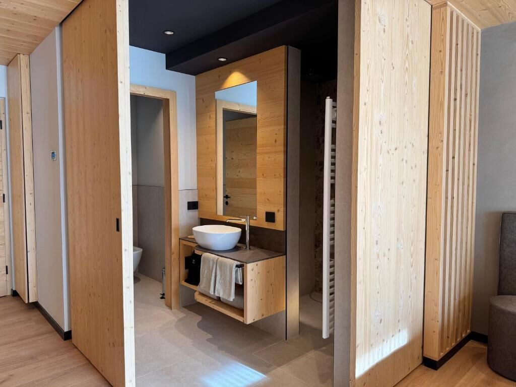 A modern bathroom with a wooden vanity, a large mirror, and a white sink.
