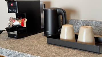 Una cafetera con dispensador de cápsulas, una máquina de café negra y dos tazas de cerámica sobre una encimera de granito.