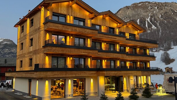 A multi-story wooden building with balconies and large windows, likely a hotel or resort, with a mountainous backdrop. - Hotel Damelis - Adults Only (Livigno)