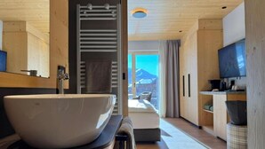 A modern bathroom with a large white basin, wooden flooring, and a view of a mountain through a large window. - Hotel Damelis - Adults Only (Livigno)