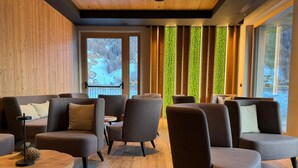 A modern lounge area with sofas and a round table, large windows with a view of a snowy landscape, and vertical wooden slats on the wall. - Hotel Damelis - Adults Only (Livigno)