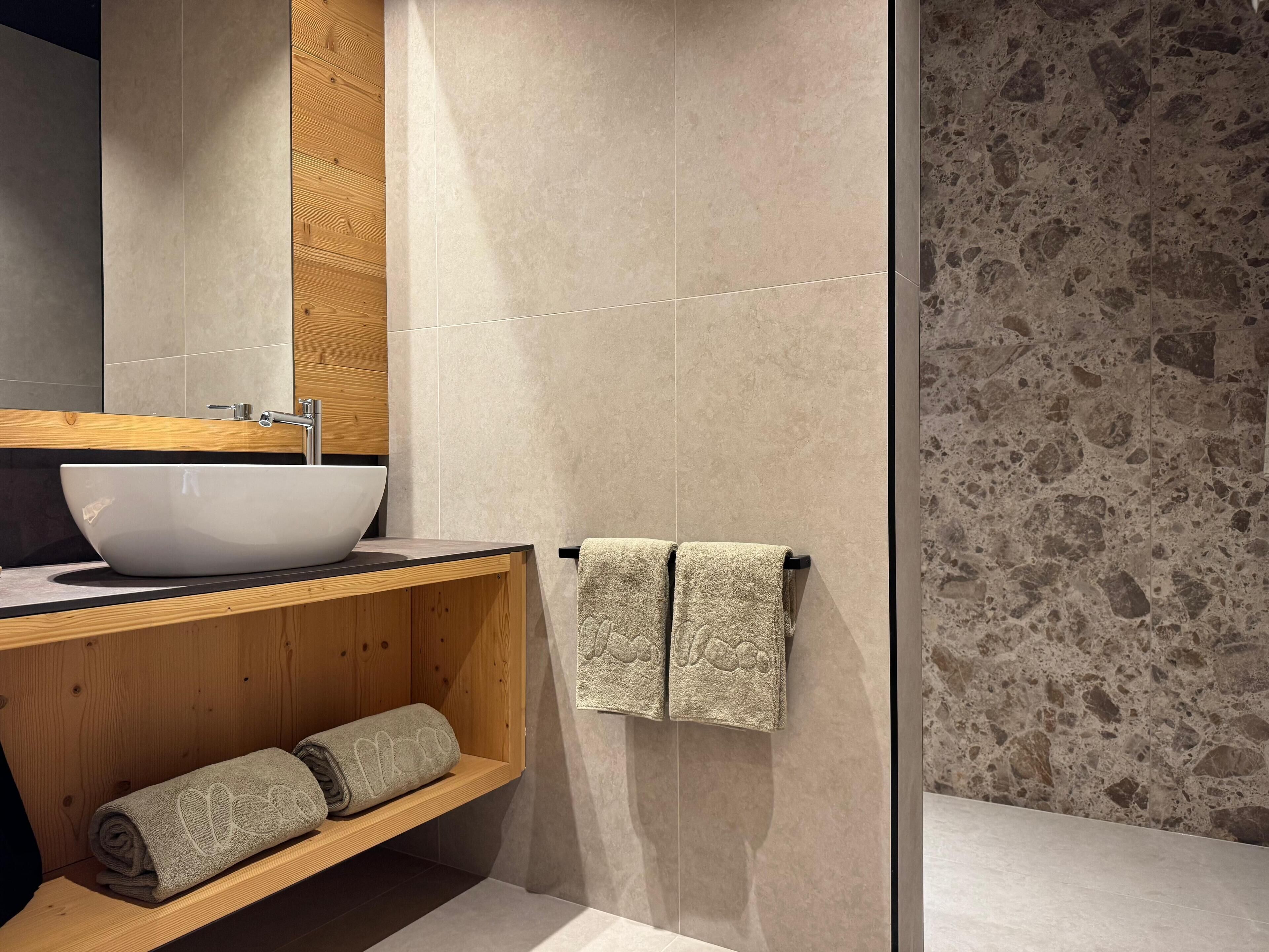 Un baño moderno con un lavabo blanco grande, tocador de madera y cabina de ducha de vidrio.