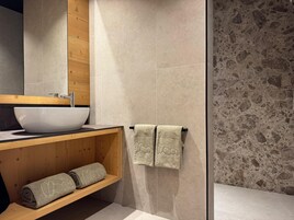 Un baño moderno con un lavabo blanco grande, tocador de madera y cabina de ducha de vidrio.