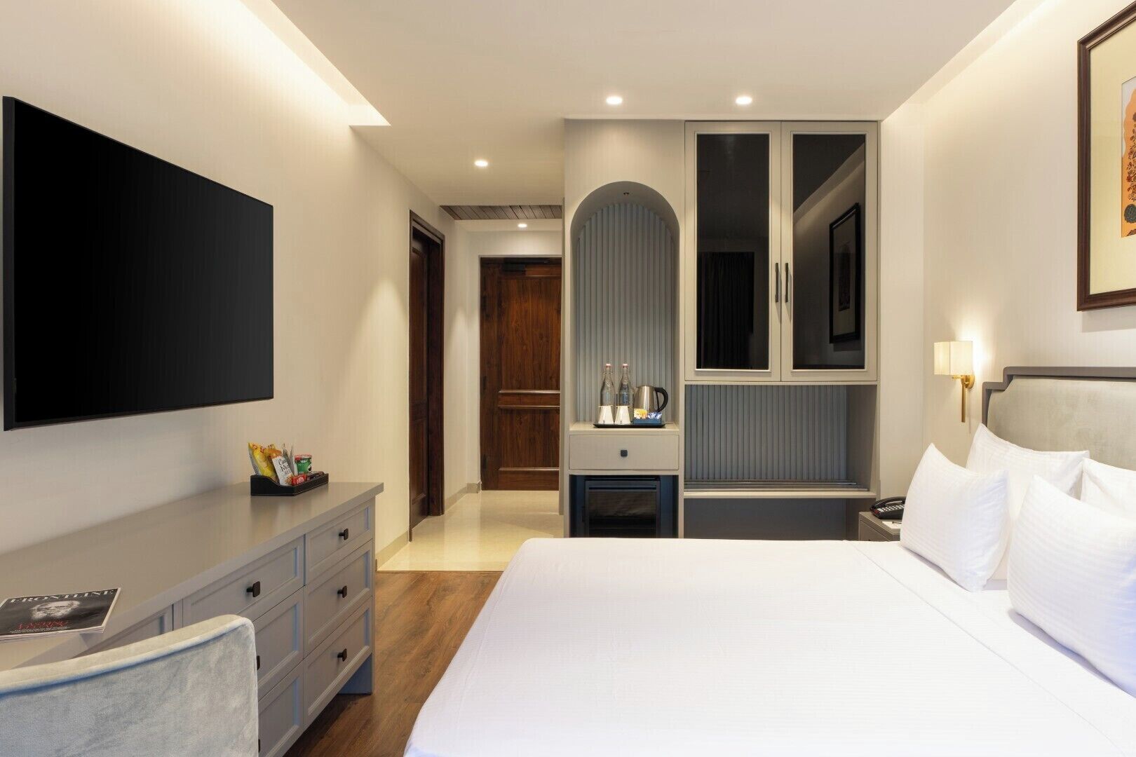Habitación de hotel moderna con una cama grande, un televisor de pantalla plana, un escritorio con cajones, una tocador con espejo y una puerta que da a otra habitación.