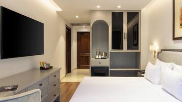 Habitación de hotel moderna con una cama grande, un televisor de pantalla plana, un escritorio con cajones, una tocador con espejo y una puerta que da a otra habitación.