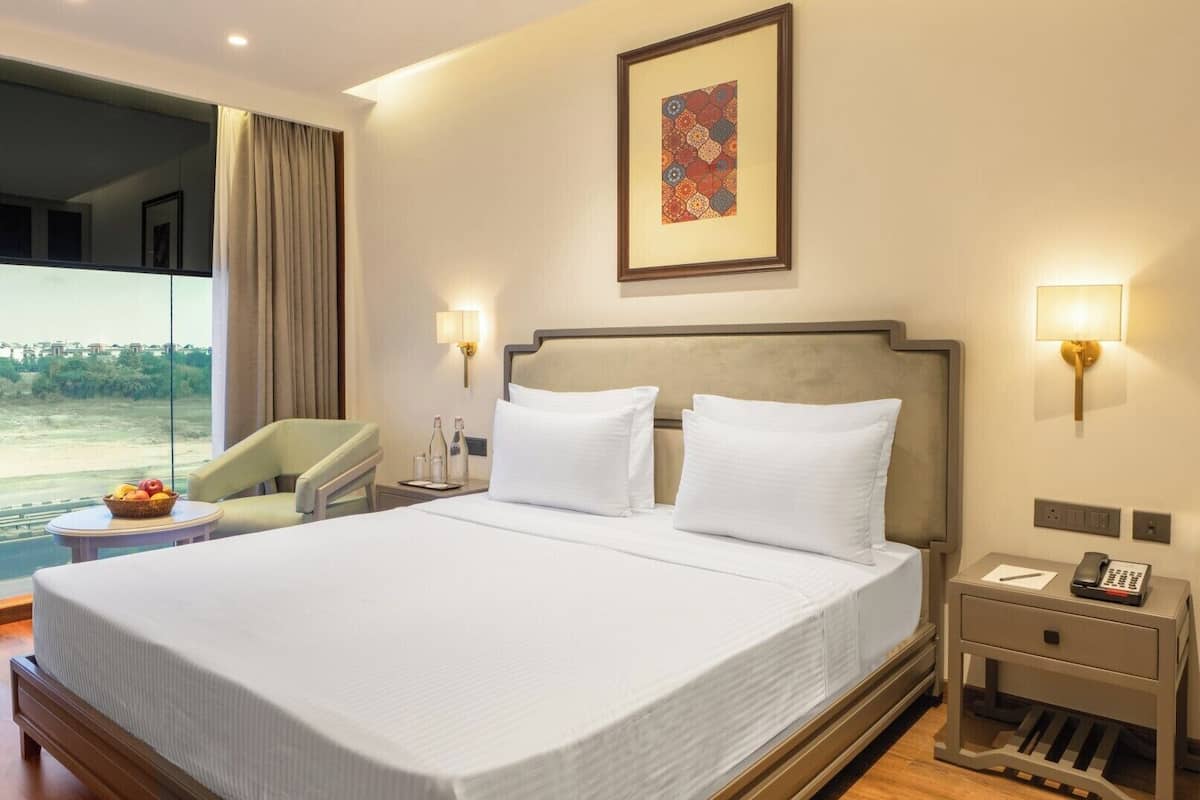 A hotel room with a large bed, two bedside tables, a chair, and a window with a view.