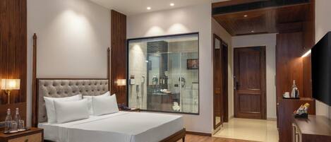 Una habitación de hotel moderna con una cama grande, paneles de madera, cabina de ducha de vidrio y un televisor sobre un mueble de madera.