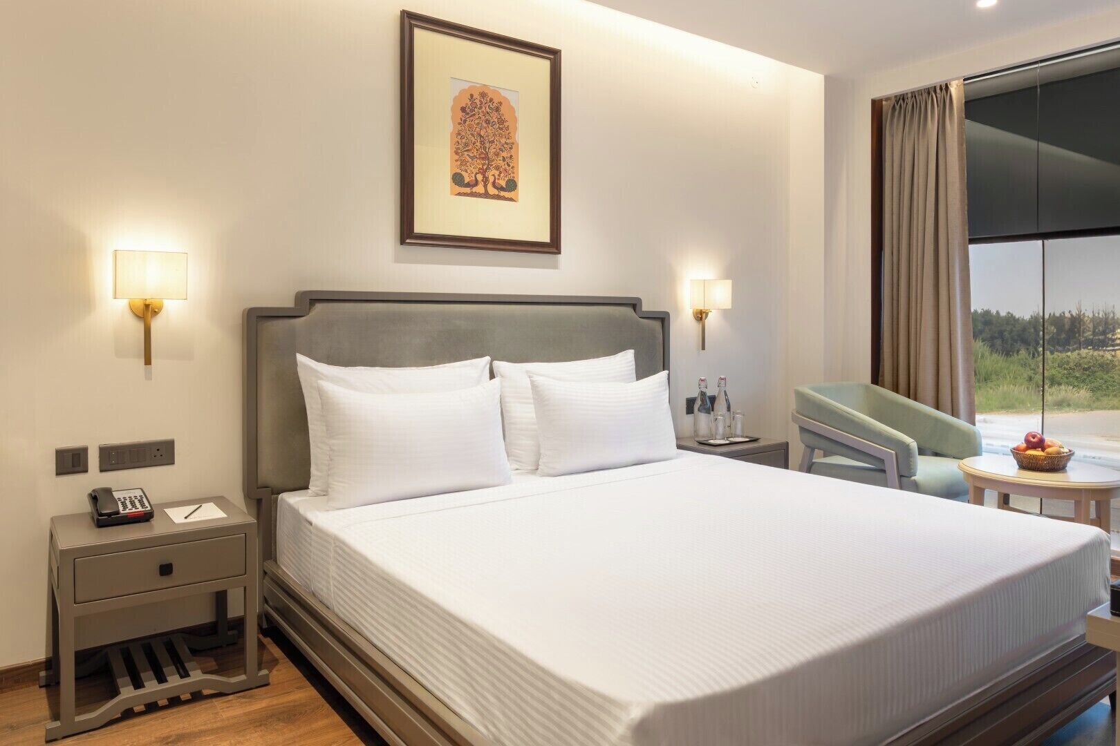 Ein Hotelzimmer mit einem großen Bett, zwei Nachttischen, einem Stuhl, einem Fenster mit Vorhängen und einem gerahmten Bild an der Wand.