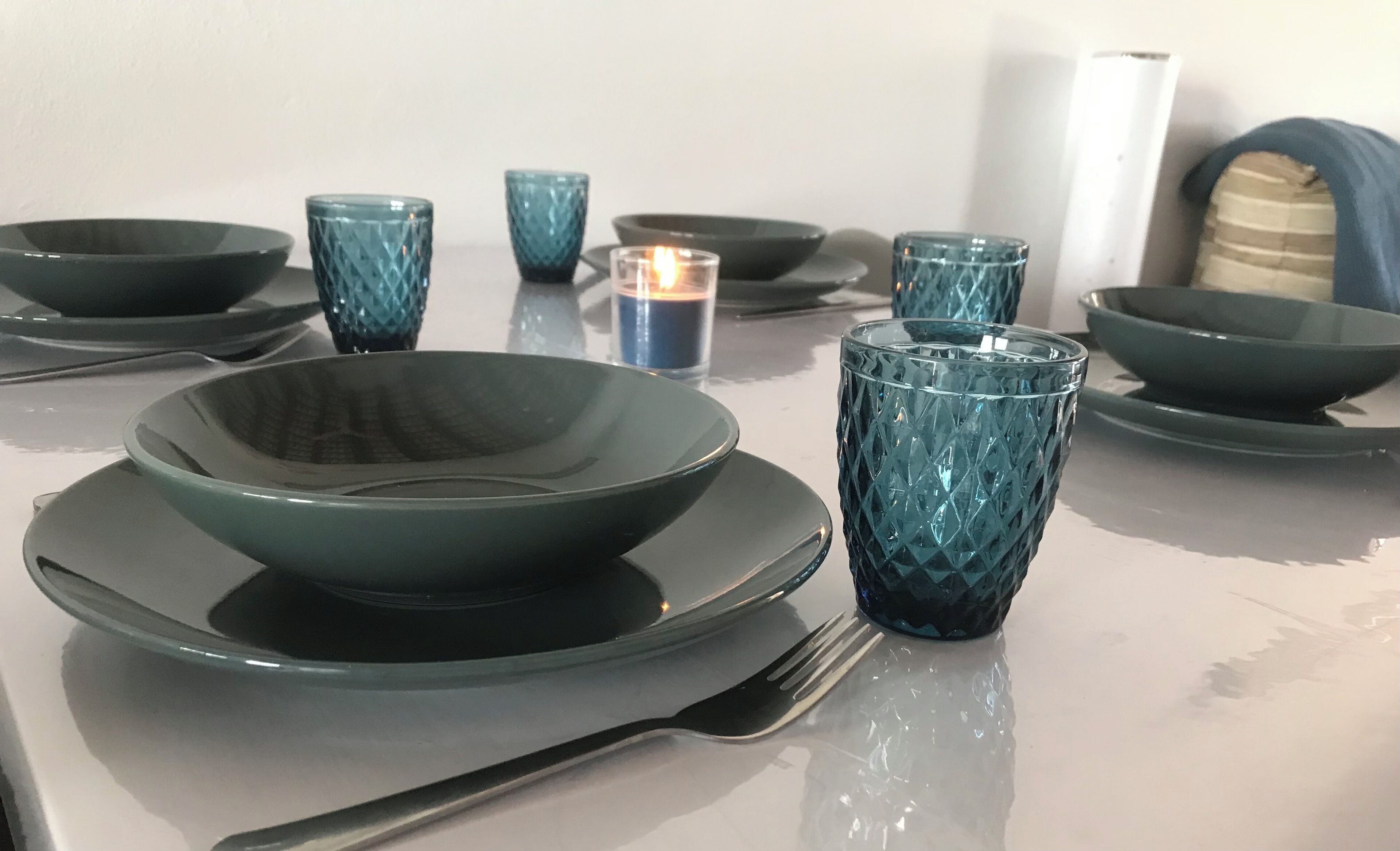 Une table dressée avec de la vaisselle et des assiettes bleu foncé, une bougie et une fourchette.