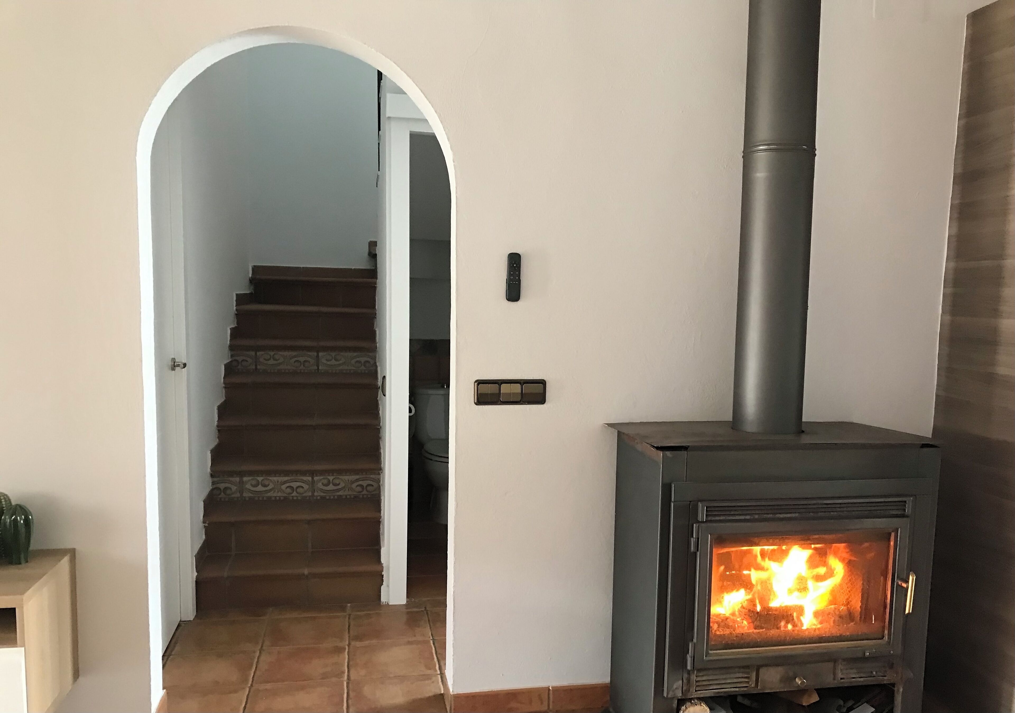 Ein Zimmer mit Kaminofen, einer Treppe zu einem weiteren Raum und einer Tür mit Lichtschalter.