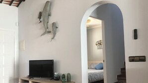 Ein Wohnzimmer mit einem Fernseher auf einem Holzboden, einer Wandskulptur und einer Tür zu einem Schlafzimmer mit Bett und Treppe.