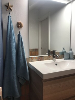 Ein Badezimmer mit einem weißen Waschbecken, einem Spiegel und zwei Handtüchern, die an Haken hängen.