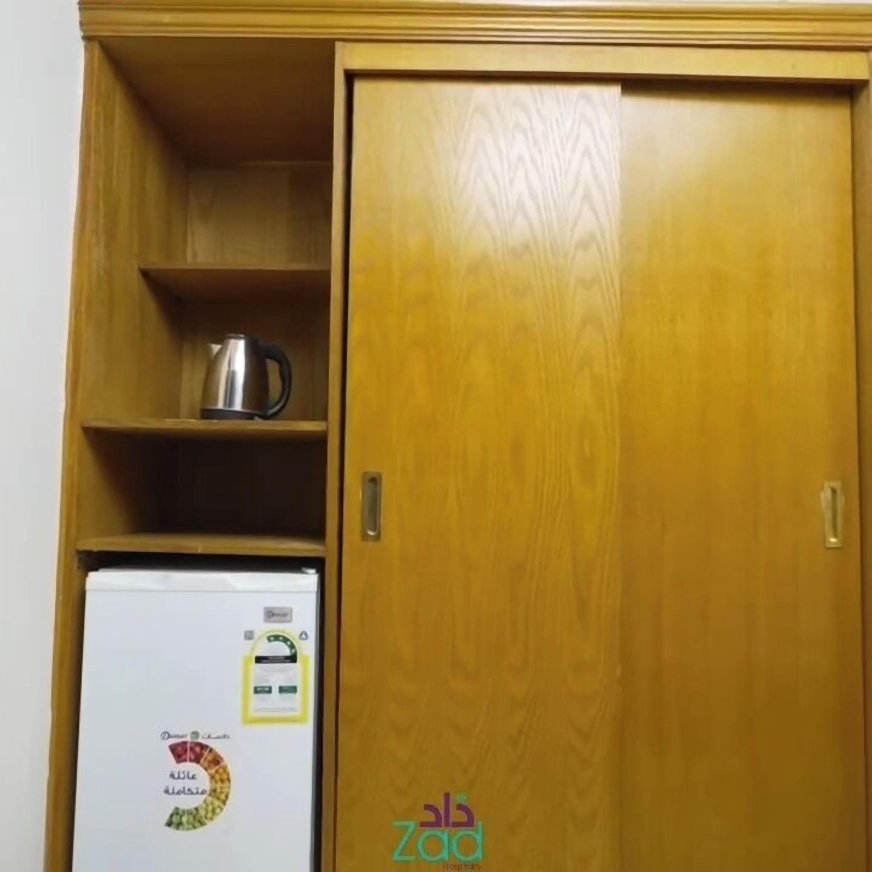 A wooden cabinet with a white refrigerator and a kettle on the shelf.