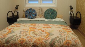 A bedroom with a floral bedspread, two patterned pillows, a nightstand, and a wall-mounted lamp. - La Casita - Apartamentos Dos Carneros (Pinos de Alhaurín)