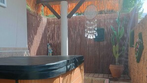 A hot tub with a wooden deck, a small step leading to it, and a bamboo fence with hanging decorations. - La Casita - Apartamentos Dos Carneros (Pinos de Alhaurín)
