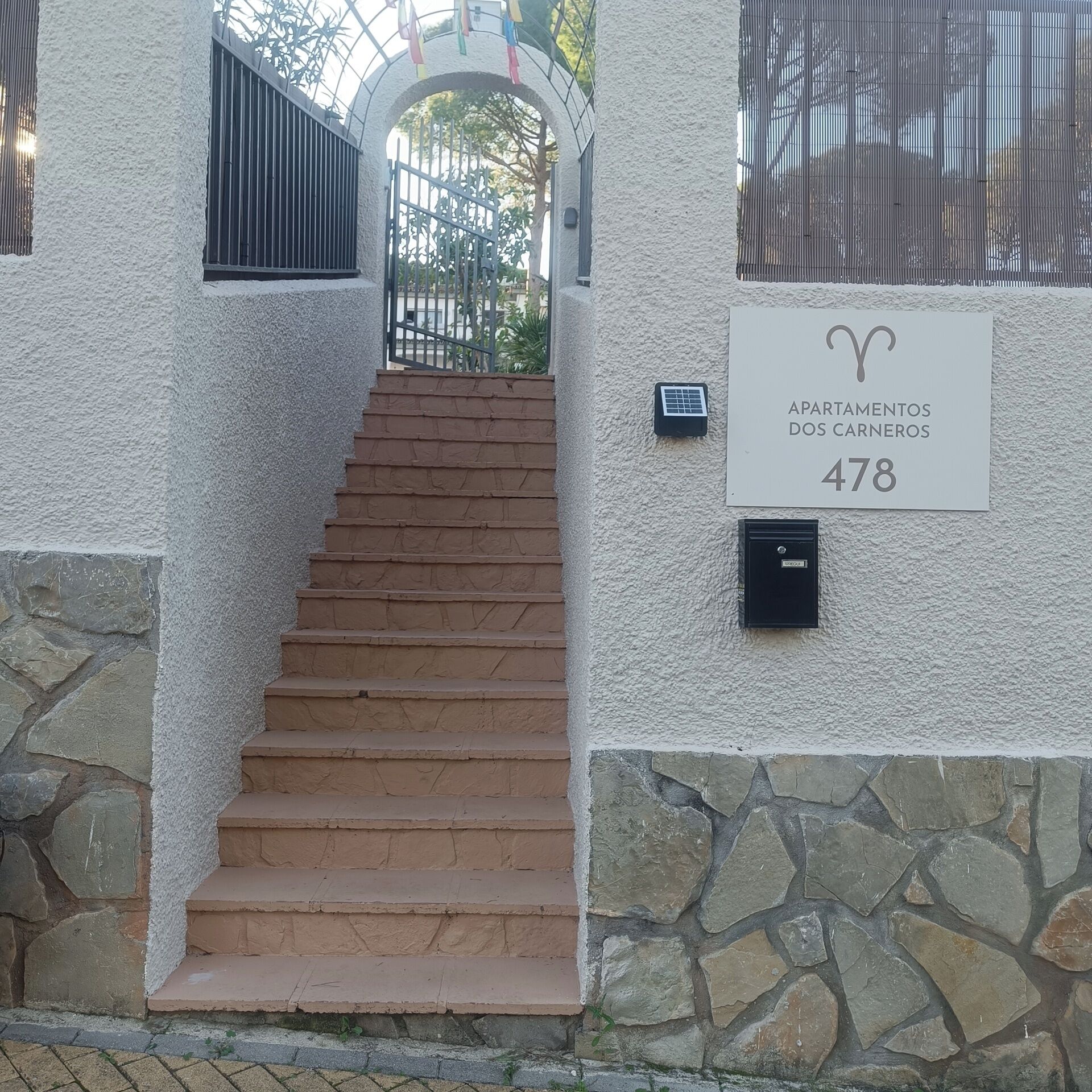 Una escalera que lleva a la entrada de un edificio, con un cartel que indica 'Apartamentos dos Carneros 478'.