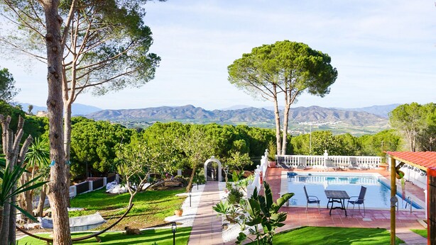 A pool area with a view of mountains, surrounded by trees and a well-maintained lawn. - La Casita - Apartamentos Dos Carneros (Pinos de Alhaurín)
