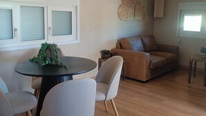 A living room with a brown leather sofa, a round table with chairs, and a decorative plant on the table. - La Casita - Apartamentos Dos Carneros (Pinos de Alhaurín)