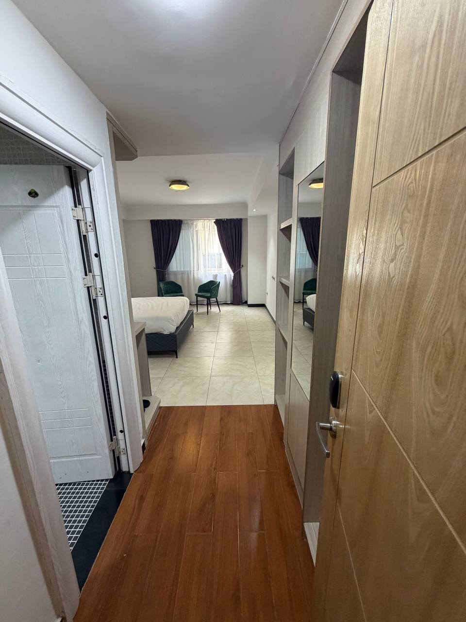 A hotel room with a wooden floor, a bed, a desk, and a wardrobe.