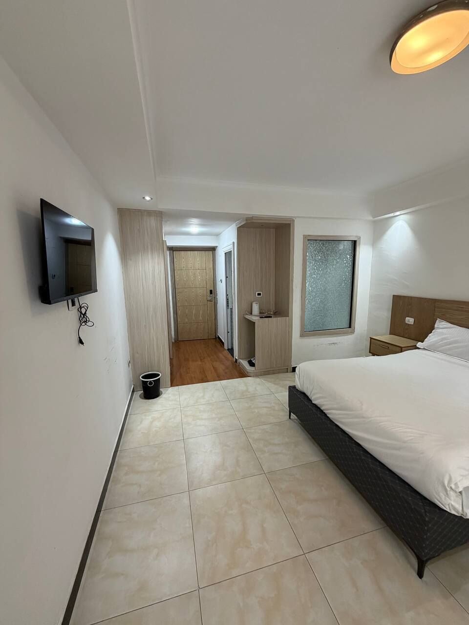 Une chambre d’hôtel avec un lit, un téléviseur fixé au mur, une fenêtre et une porte donnant sur une autre pièce.