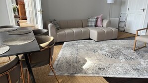 Una sala de estar moderna con un sofá modular, una mesa de comedor con sillas y una alfombra estampada.