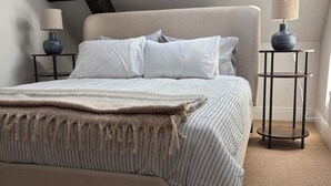 Un dormitorio con una cama, dos mesitas de noche, un ventanal y un techo inclinado.