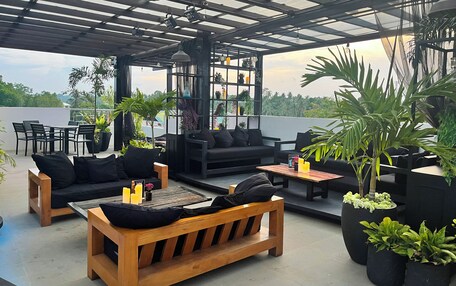 An outdoor seating area with wooden furniture, black cushions, and potted plants.