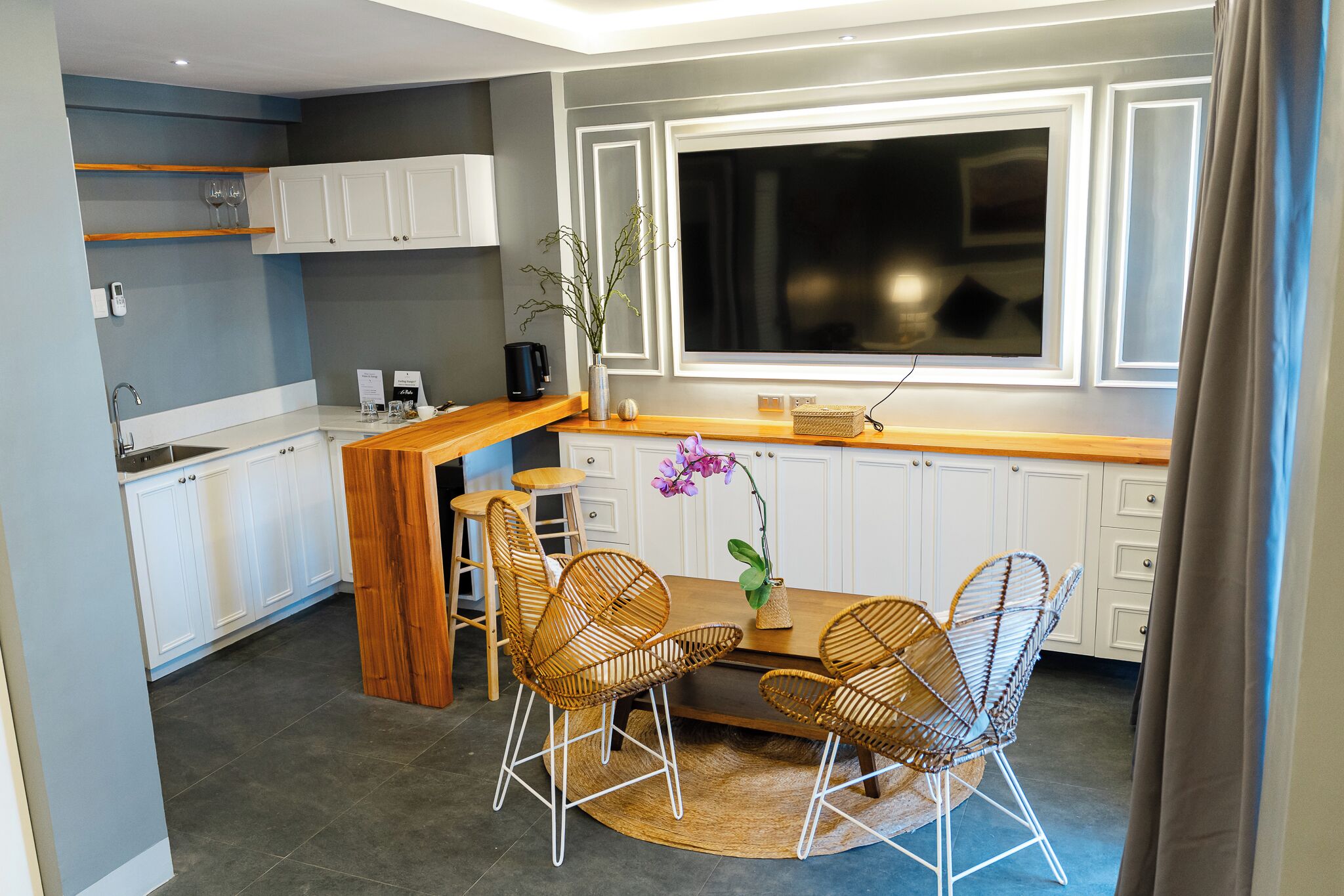 A compact kitchen with white cabinets, a wooden countertop, and a dining area with wicker chairs.