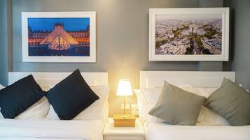 A hotel room with two beds, a nightstand with a lamp, and two framed pictures on the wall.