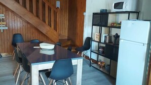Ein Zimmer mit Holzwandverkleidung, einem Esstisch, Stühlen, einer Mikrowelle, einem Kühlschrank und einem Regal mit Küchenutensilien.