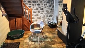Ein Zimmer mit Steinwand, einer Holztreppe, einem grünen Haustierbett, einem Sessel, einem Laufband und einer kleinen Schachtel mit Text.