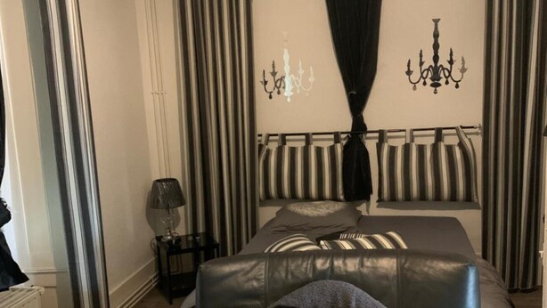 Un dormitorio con cama, mesita de noche, lámpara y ventana con cortinas.