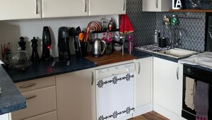 Una cocina moderna con gabinetes blancos, lavavajillas, pileta y diversos electrodomésticos.