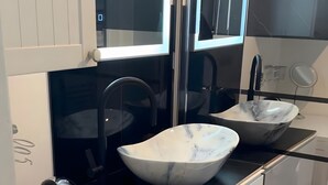 Un baño moderno con lavadora, dos lavamanos de mármol y cabina de ducha de vidrio.
