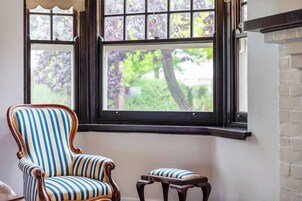 Una habitación con un ventanal grande, un sillón a rayas y un reposapiés a juego.